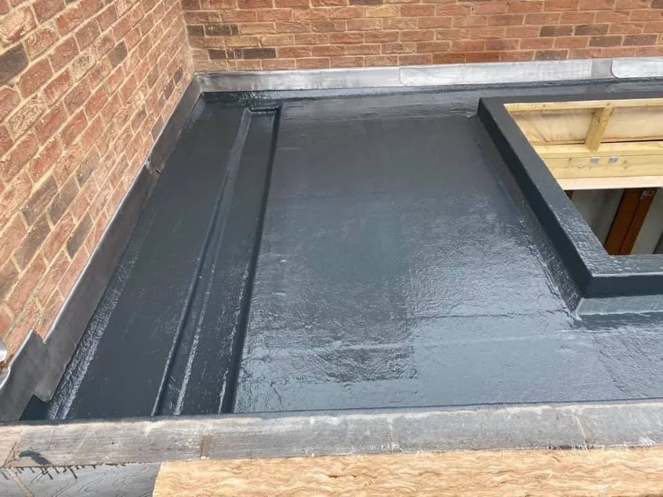 Dark grey fibreglass flat roof with upstands against brickwork